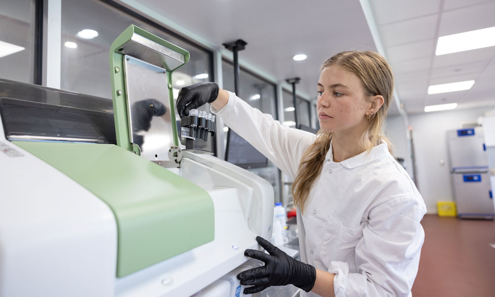 Brooklyn Becker places some small test tubes into a machine to be tested.