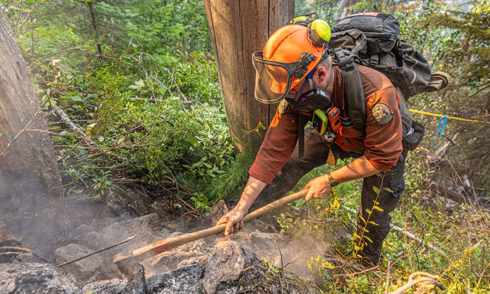 A firefighter is wearing a mask while axing at a pile of smouldering dirt.