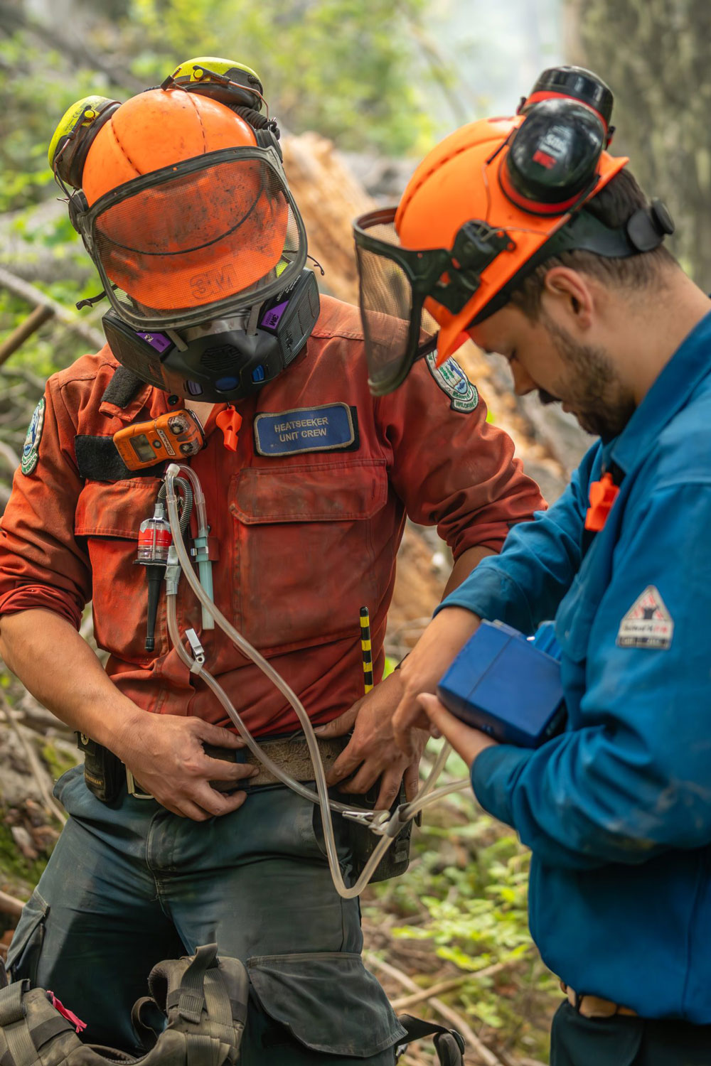 A wildland firefighter takes measurements in the field as another firefighter looks on.