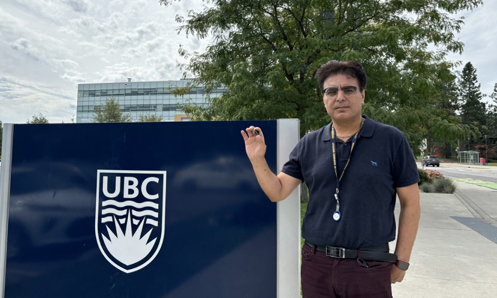 A UBCO researcher holds up a mechanical heart valve in front of a university sign