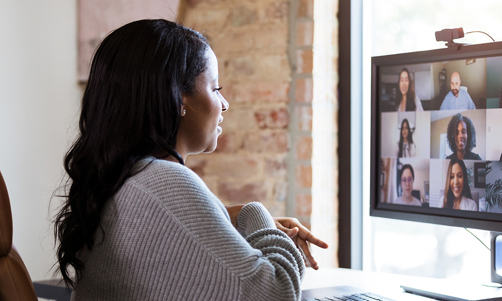 A woman with black hair and a gray sweater chats casually during a videoconference.