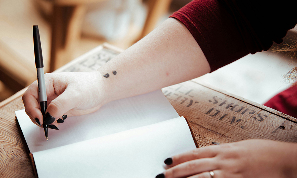 A young woman starts to write a story on a blank page of a notebook. 