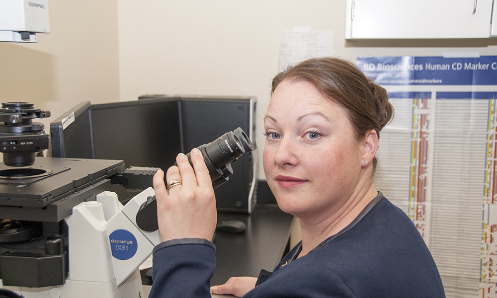 A female researcher conducts work with a mircoscope.