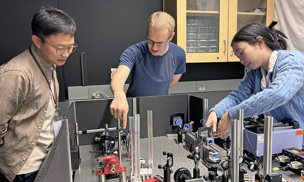 A team of researchers lean over a table covered with mechanical devices for an experiment on biological cells.