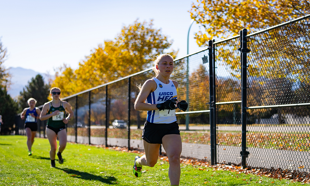 A female variety athlete leads other runners around a cross-country race course. 