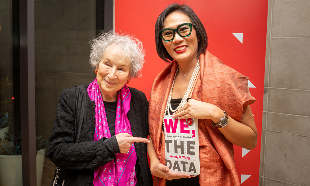 Two women, dressed for a special occasion, pose together holding an award-winning book. 